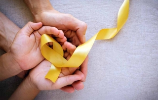 Manos sujetando una cinta amarilla por el Día del Cáncer Infantil