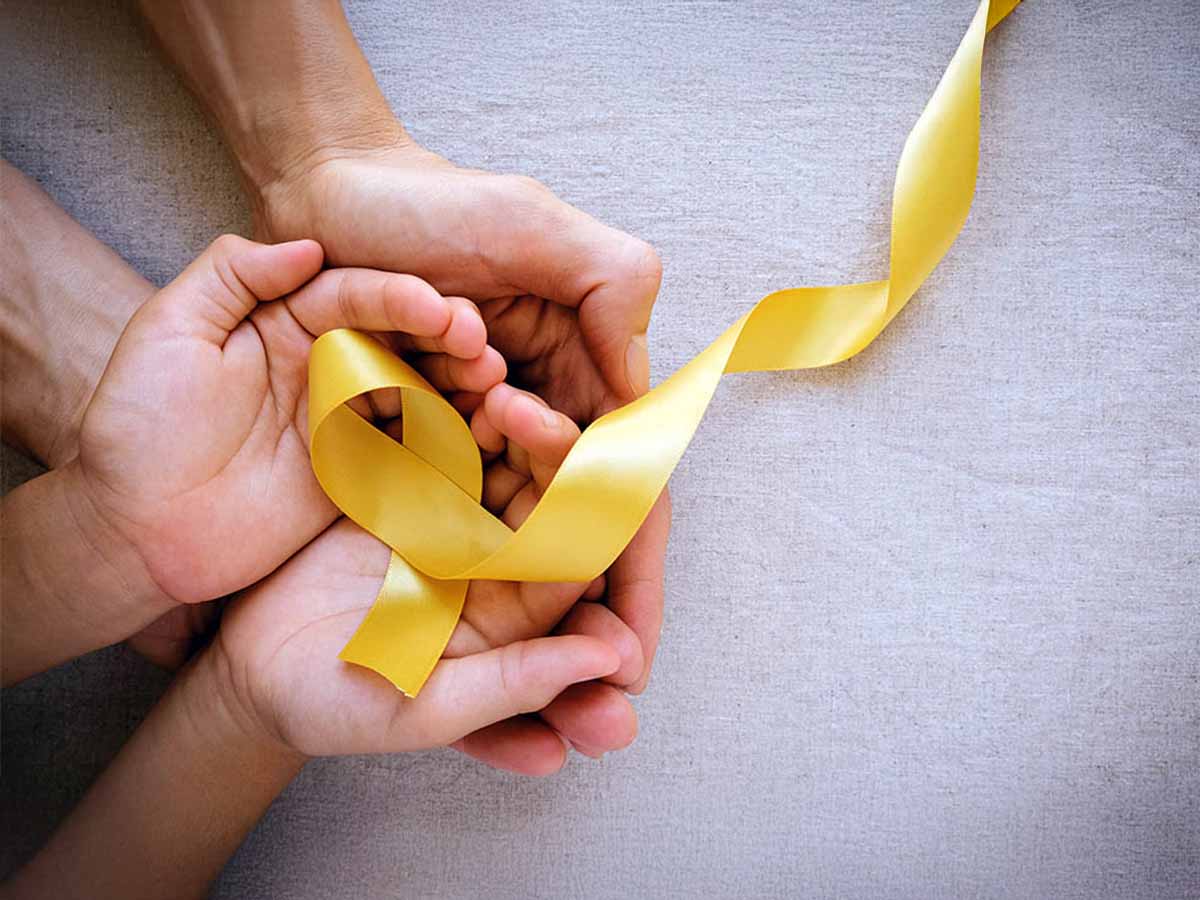 Manos sujetando una cinta amarilla por el Día del Cáncer Infantil